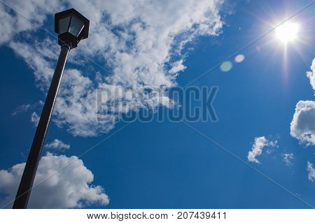 Black forged electric street lamp against a background of blue sky with clouds.