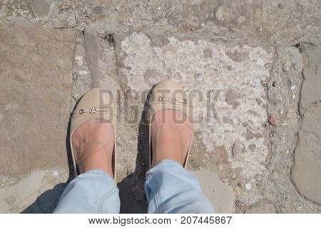 Female feet in blue jeans and ballet shoes on the cobblestone street