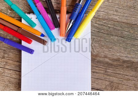Open white notepad with colorful felt-tip pens and ball pens on the wooden table. Space for text