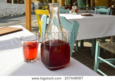 Carafe red wine and a glass filled on a table of a resturant in the center of the island of Crete
