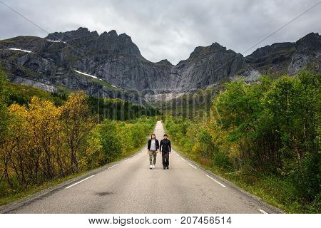 Hikers walk on a scenic road on Lofoten islands in Norway. Concept for friendship and relaxation.