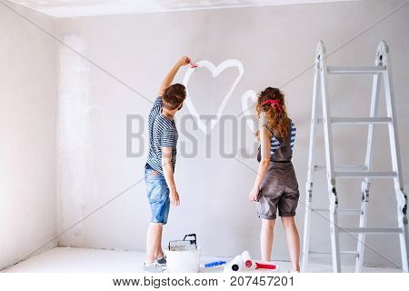 Beautiful young couple having fun and painting heart on the wall of their new house. Home makeover and renovation concept.