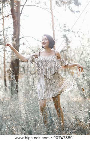 fashion styling girl is emotional. she is dressed in white with black stripes dress.forest with trees. girl in dinamic. model is running or jumping. woman in wonderland