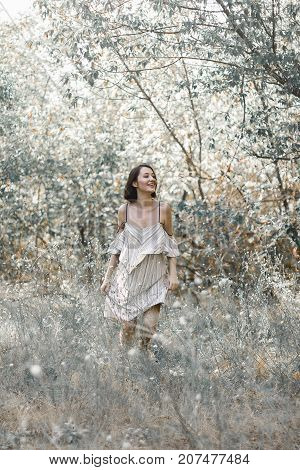 fashion styling girl is emotional. she is dressed in white with black stripes dress.forest with trees. girl in dinamic. model is running or jumping. woman in wonderland
