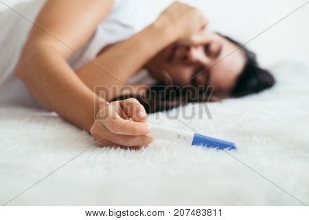 Upset woman lie sad in white bed with negative pregnancy test