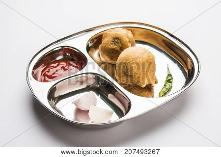 Aloo Bonda, Batata Vada or Alubonda - Indian deep fried junk but tasty food or snacks served in stainless steel plate over white background with tomato ketchup and green fried chilly, selective focus