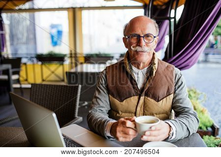 Thoughtful Senior Man With Coffee Cup Sitting At Cafe In The City