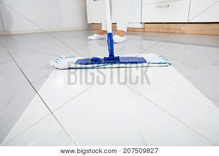 Low Section Of Person Wiping Floor With Mop In Kitchen Room