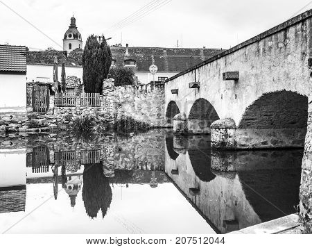 Old stone bridge reflected in calm water, Putim, Southern Bohemia, Czech Republic. Black and white image.