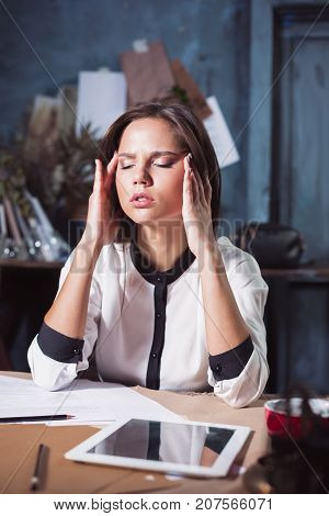 Young frustrated woman working at loft home or office desk in front of laptop suffering from chronic daily headaches