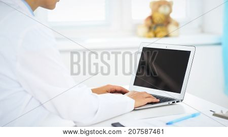 Woman doctor using laptop computer while standing straight in hospital.