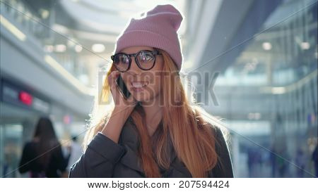 A young hipster female is talking on the phone in the big mall