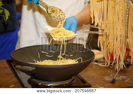 Hands in disposable blue gloves putting spagetti on a paper plate. Cooking spagetti. Fast food