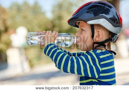 Little boy drinking water by the bike in city park