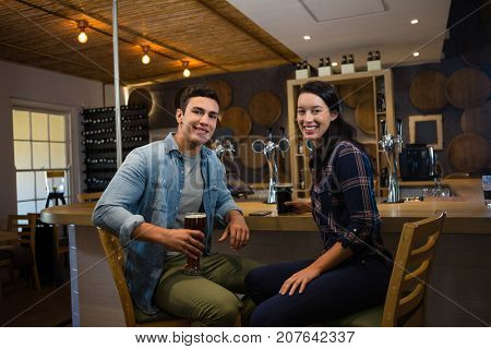 Portrait of smiling friends enjoying drinks while sitting on chairs at bar