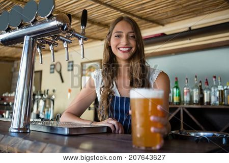 Portrait of happy young barmaid holding beer glass at restaurant