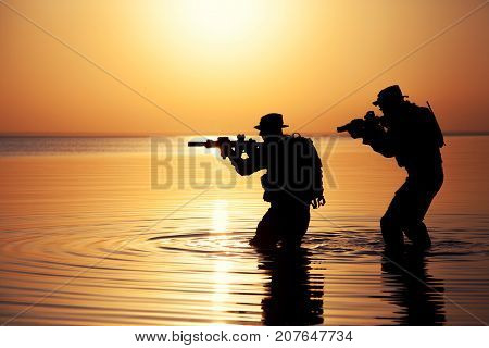 Army soldiers with rifles orange sunset silhouette in action during raid crossing river in the water