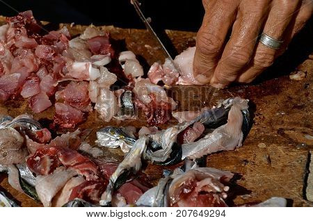 The hands op a fisherman are controlling a sharp knife which is cutting a fish in tiny parts to be used as bait.