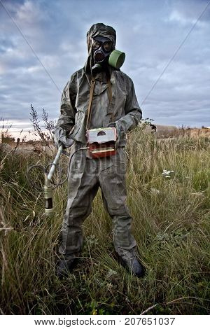 Radiation supervisor in protective clothing and gas mask with geiger counter checks the level of radiation in the radioactive zone