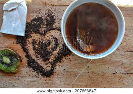 Hot tea in the cup, tea bag, tea powder hearth at the wooden background /top view
