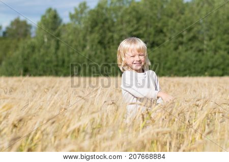 Blond Slavic happy kid boy at a ripe rye wheat field, autumn harvest, Russian forest, the Urals