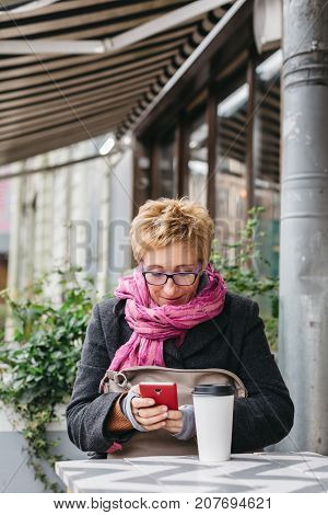 Adult pretty woman browsing smartphone in outside cafe.
