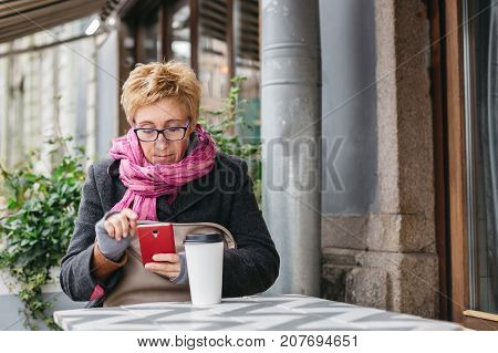 Adult pretty woman browsing smartphone in outside cafe.