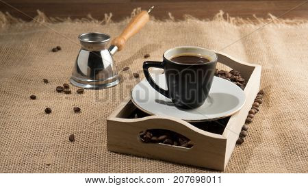 Coffee grains and cup of coffee in wooden box. Strong coffee. Coffee gezve and box on the sackcloth background. Brown image