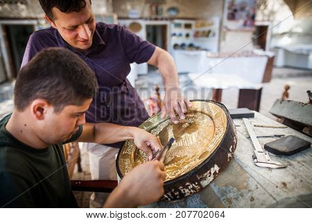 Bukhara Uzbekistan - June 4 2017: Artisans carve into metal plates in the historical city of Bukhara Uzbekistan.