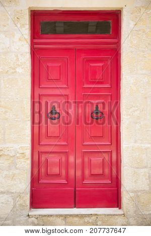 Red painted old wooden door with black iron handle in medieval city street