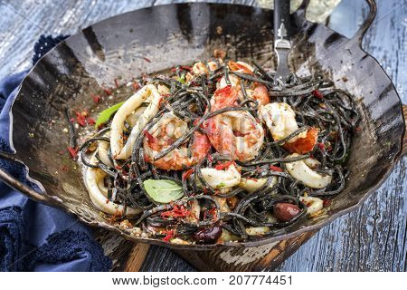 Italian linguine con tinta de calamari and prawns with olives as close-up in a wroth iron pan