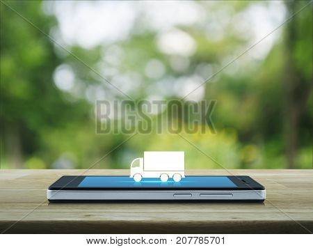 Truck flat icon on modern smart phone screen on wooden table over blur green tree in park Business transportation service concept