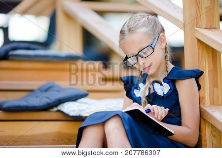 Adorable little school girl with notes and pencils outdoor.