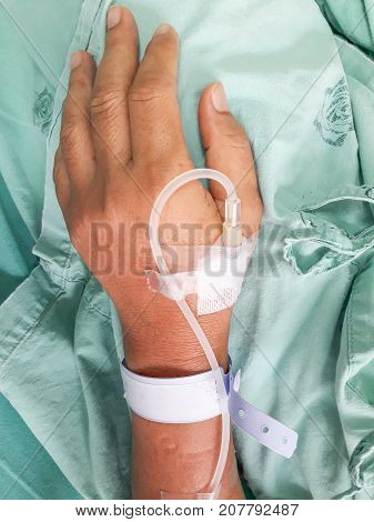 Hands of Patient is on drip receiving a saline solution on bed in hostpital.