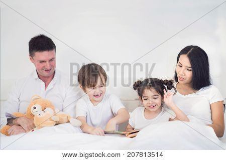 Father Mother Brothers and sister read a bedtime story togather on the bed in bedroom kid child family study education and home work concept