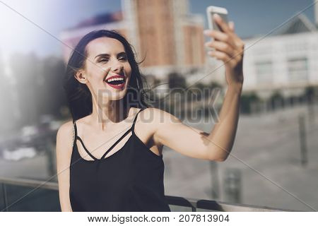 The brunette makes a salf on the background of large apartment buildings.