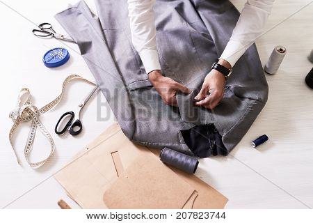 Top view of tailors table with  unrecognizable man making jacket for bespoke  suit