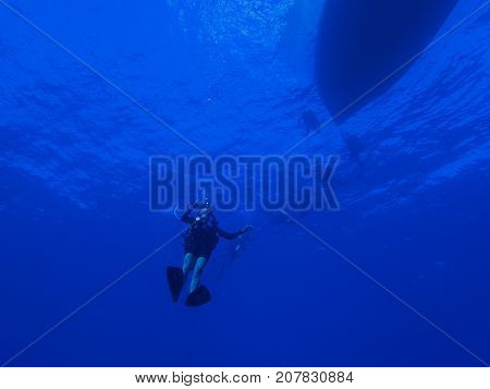 Diver Descending into the Blue Ocean with Boat Silhouette at Surface of Water