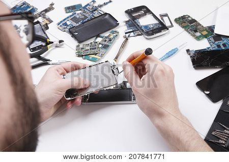 Repairman disassembling smartphone with screwdriver. Technician fixing broken phone, electronics repair service, repairer pov, copy space for text