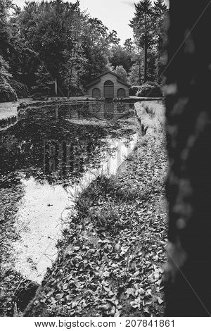 Old boat house in a tranquil ferny park with autumn leaves scattered over a charming water. A scene in the palace park 't Loo in Apeldoorn in the Netherlands