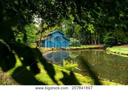 Old boat house in a tranquil ferny park with autumn leaves scattered over a charming water. A scene in the palace park 't Loo in Apeldoorn in the Netherlands