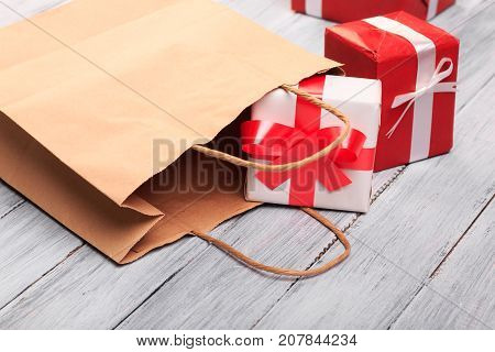 Two amazing gift boxes with colorful bow lying near a brown bag on a grey wooden parket. Close-up of gifts.