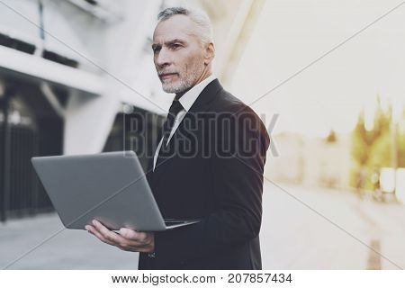Old businessman in a black suit working on laptop. He withdrew his gaze from the screen and pondered.