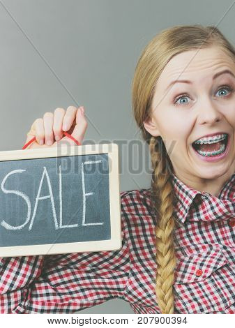 Happy crazy woman wearing checked shirt holding sign banner with sale on black board.