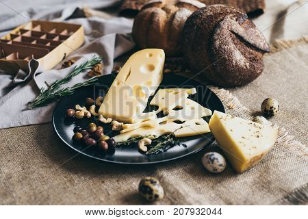 Organic healthy food prepared for cooking. Stylish set of cheese, bread, nuts, herbs and berries lying on round plate. Table decorated with beige rustic napkin. Warm atmosphere.