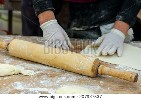 Preparing food. Human hands in gloves make dough products. Rolling pin for the dough next to it. Close-up.