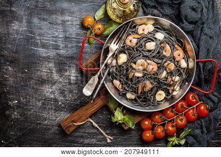 Black spaghetti with prawns and scallop in frying pan on black background, top view with copy space