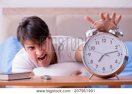 Man in bed frustrated suffering from insomnia with an alarm cloc