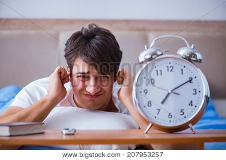 Man in bed frustrated suffering from insomnia with an alarm cloc