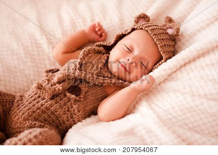 Smiling baby boy 2-3 months old wearing knitted suit sleeping in bed close up. Good morning. Childhood.